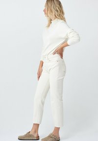 Suéter blanco ajustado de cuello alto combinado con jeans blancos de tiro alto y pierna recta. Acentuado con zapatos tipo slip-on beiges.