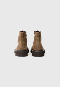 Stivaletti in suede marrone con suola in gomma spessa, dotati di chiusura con zip sul retro e tallone rinforzato.