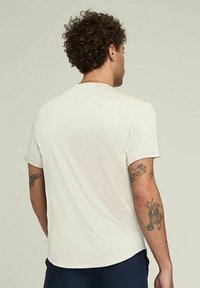 Camiseta corta de manga corta en color beige claro con cuello redondo, hecha de una tela suave; presenta una textura lisa y detalles de costura sutiles.