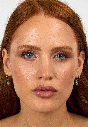 Orecchini a cerchio argento con accenti a forma di cuore, pelle liscia, labbra rosa chiaro, trucco neutro e capelli rossi lisci su uno sfondo chiaro.