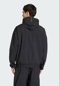 Giacca nera con cappuccio, dalla vestibilità rilassata, vita elastica e tessuto strutturato. Presenta un design minimalista e un cappuccio regolabile.