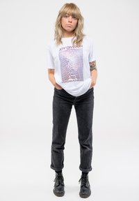 White t-shirt featuring the "Joy Division" logo and "Unknown Pleasures" graphic, paired with dark gray corduroy pants and black boots.
