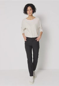 Hellbeige gestrickter Pullover mit weitem Ausschnitt, kombiniert mit schmal geschnittenen schwarzen Hosen mit Seitentaschen, getragen mit weißen Sneakers.