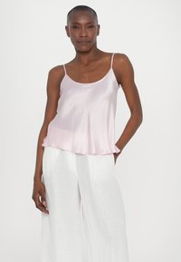 Satin rosa cami med tynne stropper og avslappet passform, med en forsiktig buet kant. Sammen med hvite linstoff bredbein bukser.