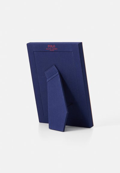 Tamsiai mėlynas nuotraukų rėmelis su tekstūruotu paviršiumi, su stoveliu gale. Raudonais rašmenimis viršuje užrašyta "POLO RALPH LAUREN".