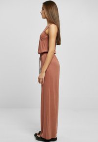 Lang, støvete rose jumpsuit med avslappet passform, ermeløs design og snøring i livet; glatt, lett stoff med en myk tekstur.