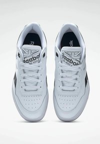 White leather sneakers with black accents, perforated toe, flat laces, padded collar, and branded tongue featuring "Reebok BB 4000 II."