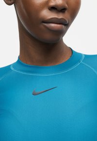 Κοντινό πλάνο ενός ατόμου που φοράει μπλε αθλητικό τοπ Nike με ορατές ραφές και μαύρο λογότυπο Nike κάτω από το λαιμό.