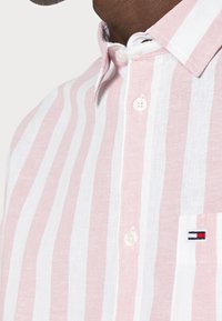 Camicia a righe in lino rosa e bianco con colletto button-down, dotata di un piccolo logo ricamato sulla tasca del petto.