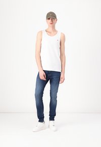 Débardeur en coton blanc, jeans moulants bleus et baskets blanches, assortis à une casquette de baseball grise. Design simple sans motifs visibles.