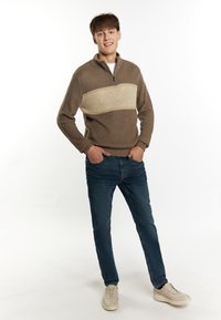 Lichtbruine zip-up trui met een crèmekleurige horizontale streep, gecombineerd met blauwe jeans en beige sneakers, met ribbelstructuur en een aangesloten ontwerp.