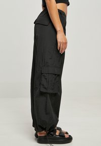 Czarne spodnie cargo wykonane z lekkiego, teksturowanego materiału z kieszeniami po bokach oraz paskiem z troczkiem, w połączeniu z czarnymi sandałami.