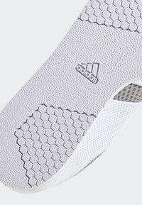 Suela de zapatilla Adidas con un material blanco texturizado, un patrón hexagonal, un logo en relieve y acentos de malla cerca del borde.