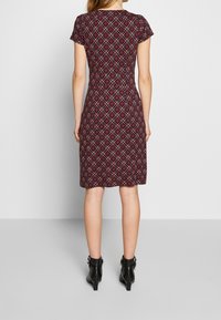 Abito a pois color marrone con maniche corte, design aderente e lunghezza media; indossato con stivaletti neri con tacco.