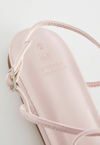 Vaaleanpunaiset sandaalit pehmeästä materiaalista, ohuilla remmeillä ja teksturoitu pohja, jossa lukee "IKUISEN MUKAVUUDEN", koko 6½/40.