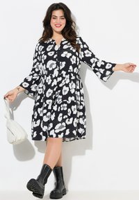Schwarzes und weißes Leopardenmuster-Kleid mit lockerer Passform, Glockenärmeln, durchgehender Knopfleiste und schichtweise Gestaltung. Kombiniert mit schwarzen Ankle Boots und einer weißen Tasche.