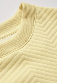 Maglione giallo con un col ribattuto e un motivo a zigzag testurizzato su tutta la stoffa. Materiale in cotone morbido con una finitura liscia.