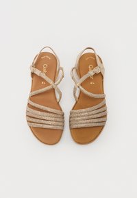 Sandali color tan con molte cinghie incrociate in oro, dotati di chiusura con fibbia. Parte superiore liscia e soletta ammortizzata per il comfort.