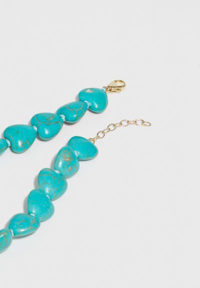 Οβάλ κοχύλια σε ιριδίζουσα απόχρωση, συνδεδεμένα με χρυσό υλικό και αλυσίδα επέκτασης για ρυθμιζόμενο μήκος.