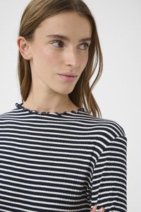 Gestreiftes Oberteil in Marineblau und Weiß mit gerippter Struktur, ausgestattet mit einem gerüschten Rundhalsausschnitt. Das Model hat glattes Haar und kleine Ohrstecker.