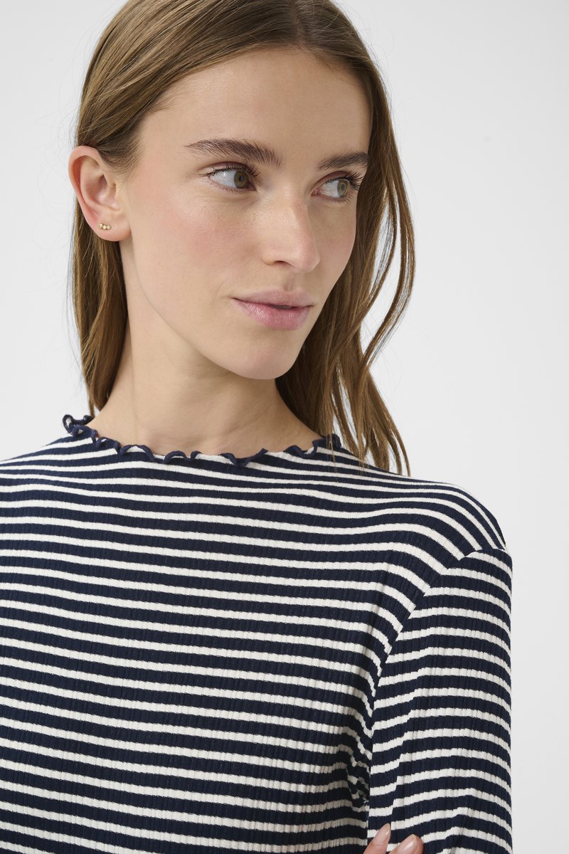 Gestreiftes Oberteil in Marineblau und Weiß mit gerippter Struktur, ausgestattet mit einem gerüschten Rundhalsausschnitt. Das Model hat glattes Haar und kleine Ohrstecker.