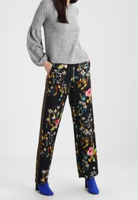 Blommiga byxor med vida ben i svart bas med flerfärgade blommor. Mjuk tyg, kombinerat med en grå tröja och blå skor.