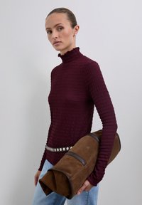 Maroon textured turtleneck sweater with ruffled collar, paired with light blue jeans and a brown suede cylindrical bag with dark accents.