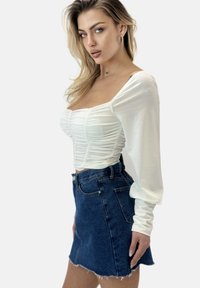 Top bianco aderente con dettagli arricciati e maniche lunghe abbinato a una mini gonna in denim scuro a vita alta con orlo grezzo e tasche frontali.