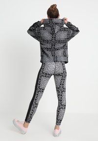 Conjunto de sudadera y leggings en blanco y negro con un diseño de paisley, de forma ajustada y con tela texturizada. El conjunto se combina con unos zapatos rosas.