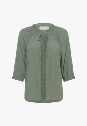 Gaiši zaļa blūze ar apaļu kakla izgriezumu, saites detaļu, 3/4 garuma piedurknēm un teksturētu centrālo paneļu, kas ar pinuma dizainu. Mīksta auduma, brīva piegriezuma.