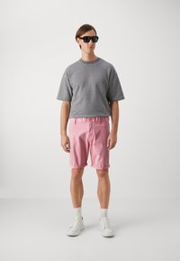 Grå kortermet sweatshirt, lyserosa rullet shorts, hvite sneakers og svarte solbriller. Enkel, avslappet passform med glatte teksturer.