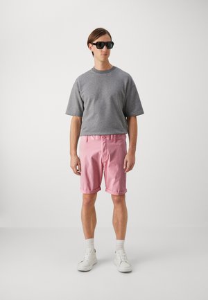 Sudadera gris de manga corta, pantalones cortos enrollados de color rosa claro, zapatillas blancas y gafas de sol negras. Estilo sencillo y relajado con texturas suaves.