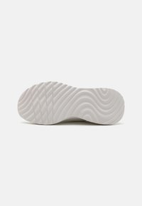 Semelle d'une basket, avec une texture ondulée en caoutchouc gris clair, comportant des rainures horizontales pour l'adhérence et une finition lisse dans l'ensemble.