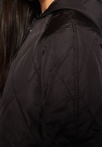 Schwarze gesteppt Jacke mit Kapuze; bietet eine glatte Textur und ein Rautenmuster. Enthält Nahtdetails an der Schulter.