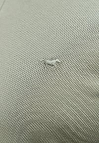 Jasnoszara tkanina o teksturze z małym, wyszywanym wzorem psa. Tło ukazuje pleciony wzór, podkreślający jakość materiału.