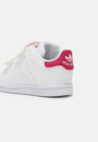 Baltas ādas sporta apavi ar struktūru, rozā akcentiem uz papēža, perforētiem elementiem un gumijas zoli. Logo uz papēža. 