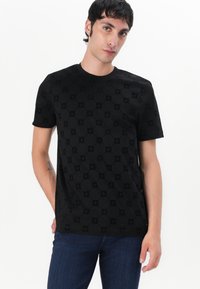 T-shirt noire à manches courtes avec un motif texturé à motifs circulaires, fabriqué en matériau doux, associé à un jean bleu.