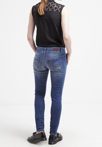 Blå denim skinny jeans har en medelhög midja, traditionell fem-fickasdesign och subtila blekningar. Kombineras med en svart ärmlös topp.