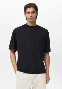 Czarny bawełniany t-shirt z okrągłym wycięciem, krótkimi rękawami i kieszonką na piersi, cechujący się luźnym krojem i gładką fakturą.