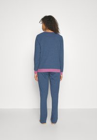 Blauw langwerpig shirt met een frambozen-gestreepte onderrand en bijpassende broek. Zachte stof, relaxte pasvorm en iets losse stijl.