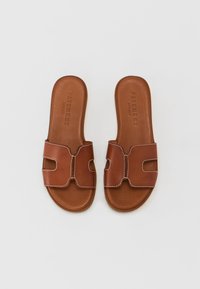 Brown leather slide sandals featuring two cutout straps with contrasting stitching, flat sole, and embossed brand logo on the footbed.