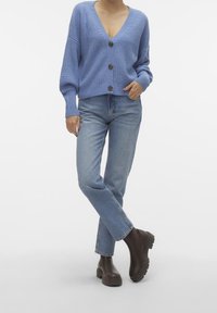 Jasnoniebieski dziergany sweter na guziki z dekoltem w serek, w połączeniu z jasnoniebieskimi dżinsami o prostych nogawkach oraz ciemnobrązowymi masywnymi botkami na kostkę.