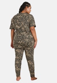 Svart och beige mönstrad jumpsuit med korta ärmar, med abstrakta leopard- och vågmönster, figurnära silhuett och stretchig tyg.