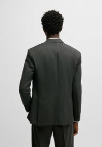 Giacca di abito grigio scuro con righe, dal taglio sartoriale, con una fessura singola e rever a lancia. Realizzata in tessuto testurizzato con una leggera lucentezza.