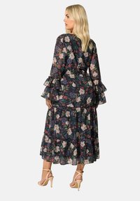 Vestido maxi floral con largas mangas transparentes, puños con volantes y dobladillo en capas. Fondo oscuro con rosas, violetas y hojas verdes.