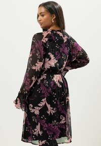 Svart blommig klänning med genomskinligt tyg, prydd med stora lila och rosa snurrande mönster, långa ärmar och en samla i midjan.