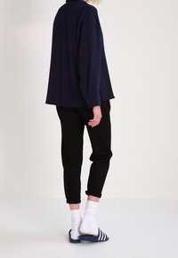 Camisa de color navy con un corte holgado, combinada con pantalones negros. Calcetines blancos y sandalias de tiras a rayas navy. Tejido suave y puños enrollados visibles.
