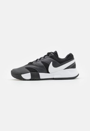 Baskets Nike noires et grises avec logo swoosh blanc et semelle blanche épaisse, montrées en profil droit sur fond blanc uni.