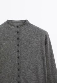 Cardigan gris en tricot avec un col montant, comportant sept boutons noirs sur le devant. Texture douce et coupe décontractée.
