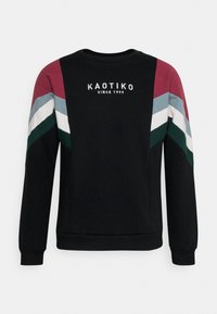 Sudadera negra con rayas en forma de chevron en color burdeos, azul, blanco y verde en las mangas y el texto "KAOTIKO SINCE 1999" en el centro del frente.